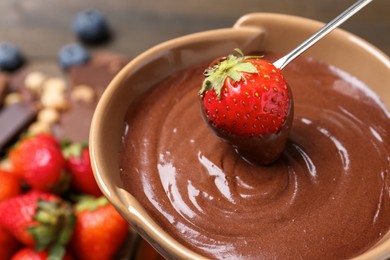 Photo of Dipping fresh strawberry in fondue pot with melted chocolate at table, closeup