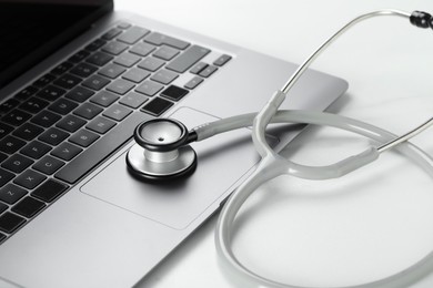 Photo of Modern laptop and stethoscope on white table, closeup