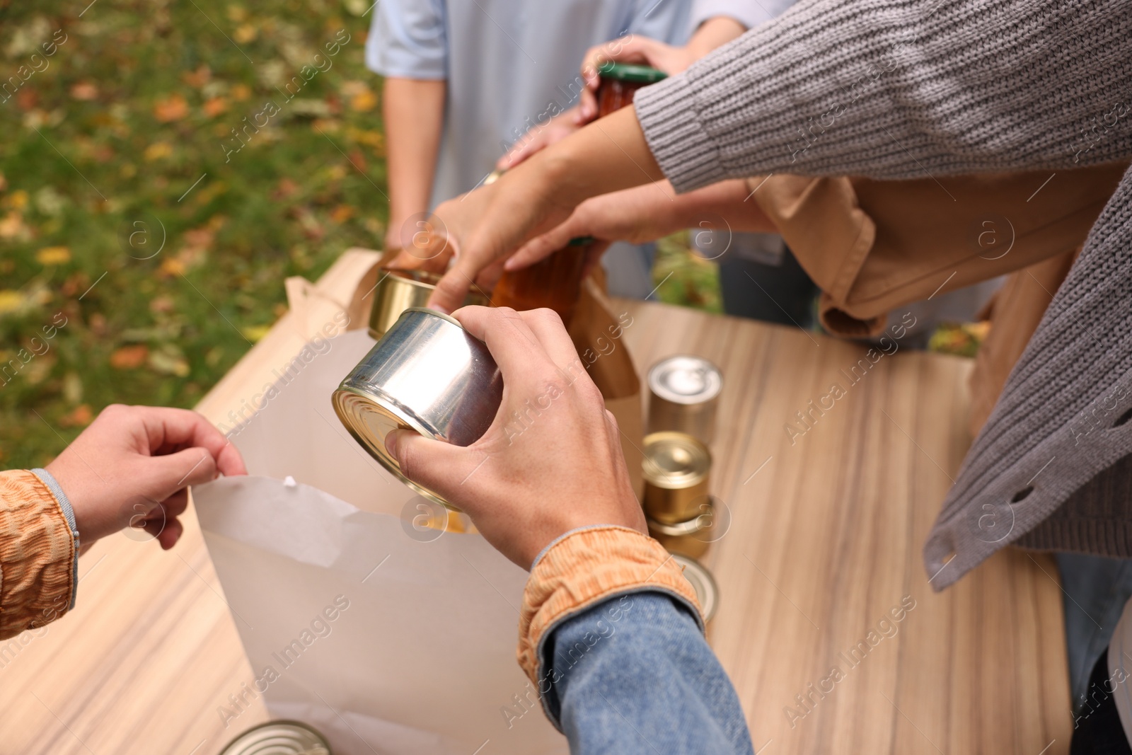 Photo of Group of volunteers packing food products at table outdoors, closeup