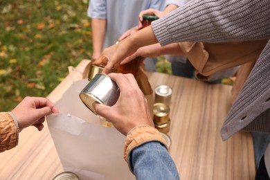 Photo of Group of volunteers packing food products at table outdoors, closeup