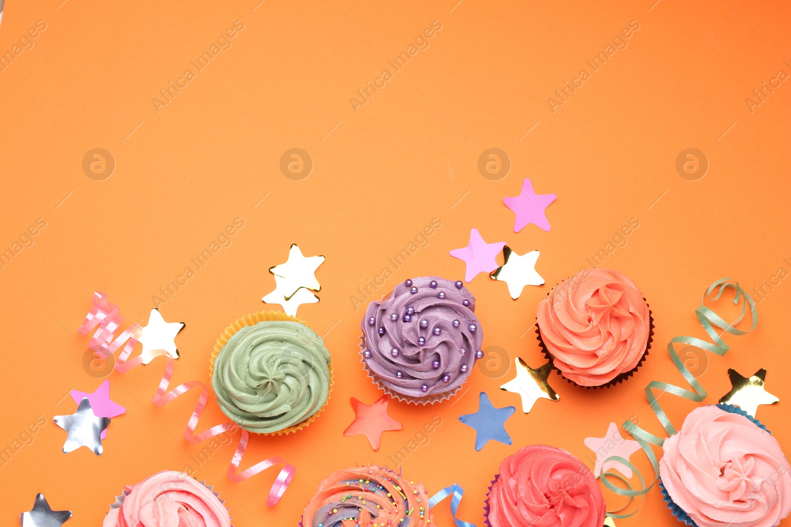 Photo of Delicious cupcakes with bright cream and party decor on orange background, flat lay. Space for text