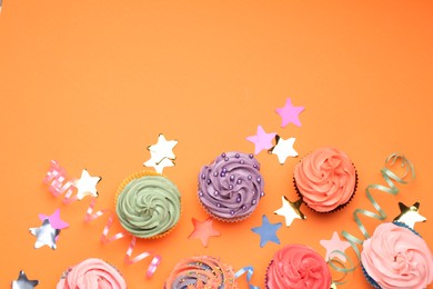 Photo of Delicious cupcakes with bright cream and party decor on orange background, flat lay. Space for text