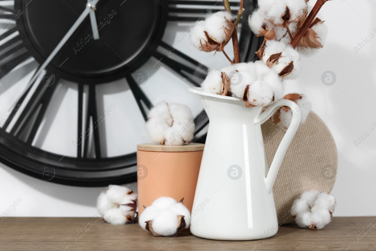 Photo of Cotton branches with fluffy flowers and home decor on wooden table near white wall