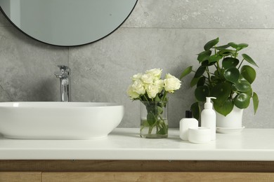 Beautiful roses, houseplant and bath accessories near sink in bathroom