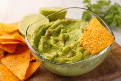 Bowl of delicious guacamole served with nachos chips and lime on wooden board, closeup
