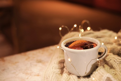 Cup of hot mulled wine and garland on table against blurred background. Space for text