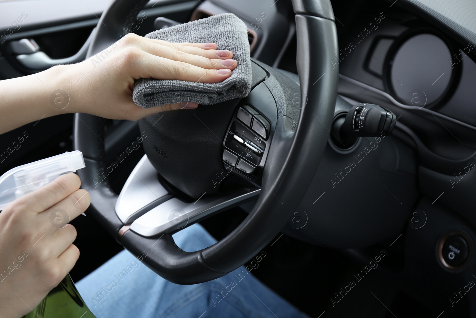 Photo of Woman cleaning steering wheel with rag in car, closeup