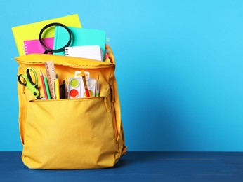 Yellow backpack with different school stationery on blue wooden table, space for text
