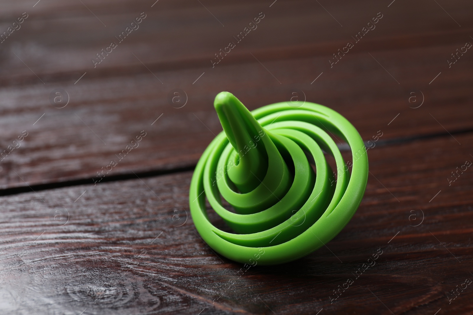 Photo of One green spinning top on wooden table, closeup. Space for text