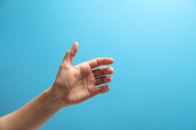 Woman holding something in hand on light blue background, closeup. Space for text