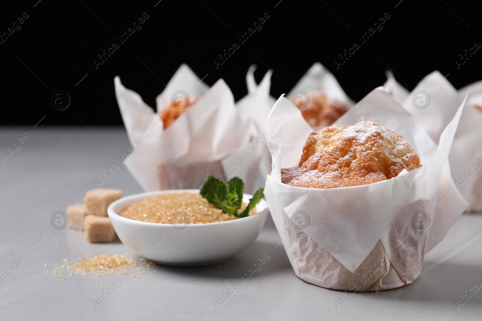 Photo of Delicious muffins with powdered sugar on grey table, closeup