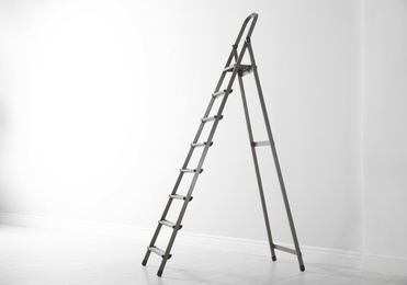 Photo of Modern metal stepladder near white wall. Space for text