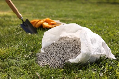 Photo of Granulated fertilizer in sack on green grass outdoors, closeup. Space for text