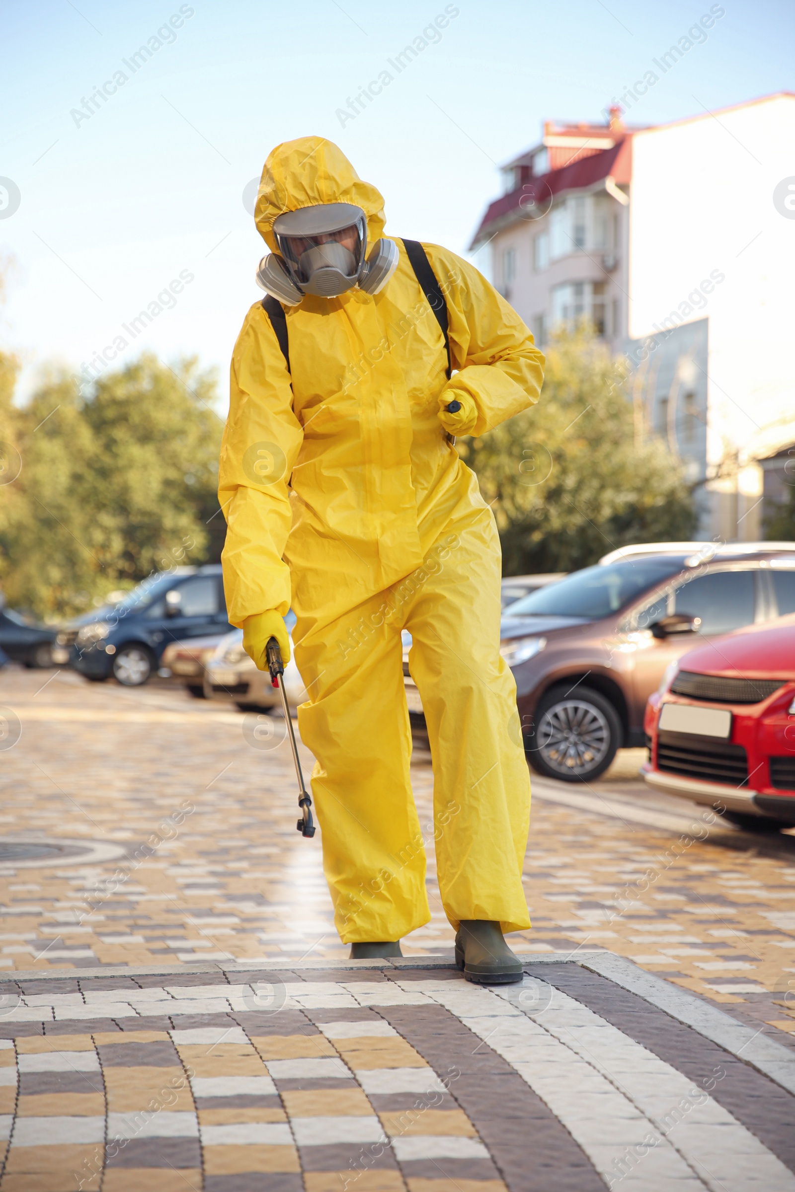 Photo of Person in hazmat suit disinfecting street with sprayer. Surface treatment during coronavirus pandemic