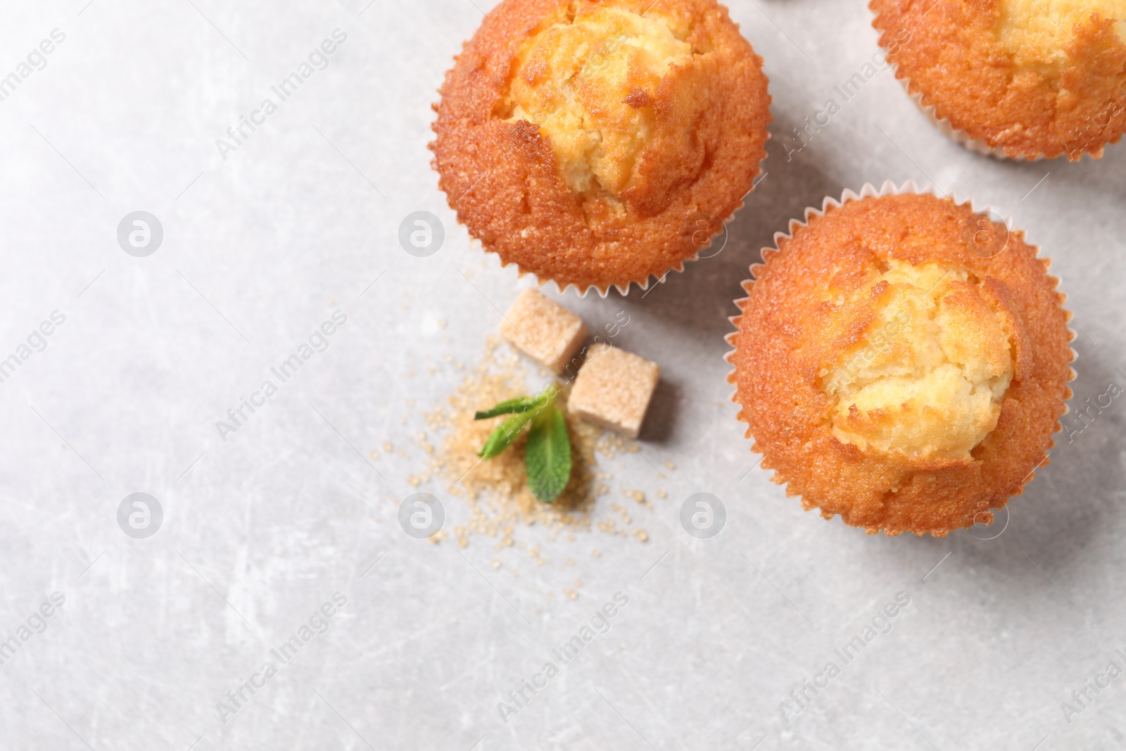 Photo of Delicious sweet muffins and brown sugar on light grey textured table, flat lay. Space for text