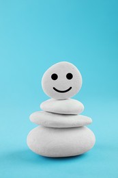 Photo of Stack of stones with drawn happy face on light blue background. Zen concept
