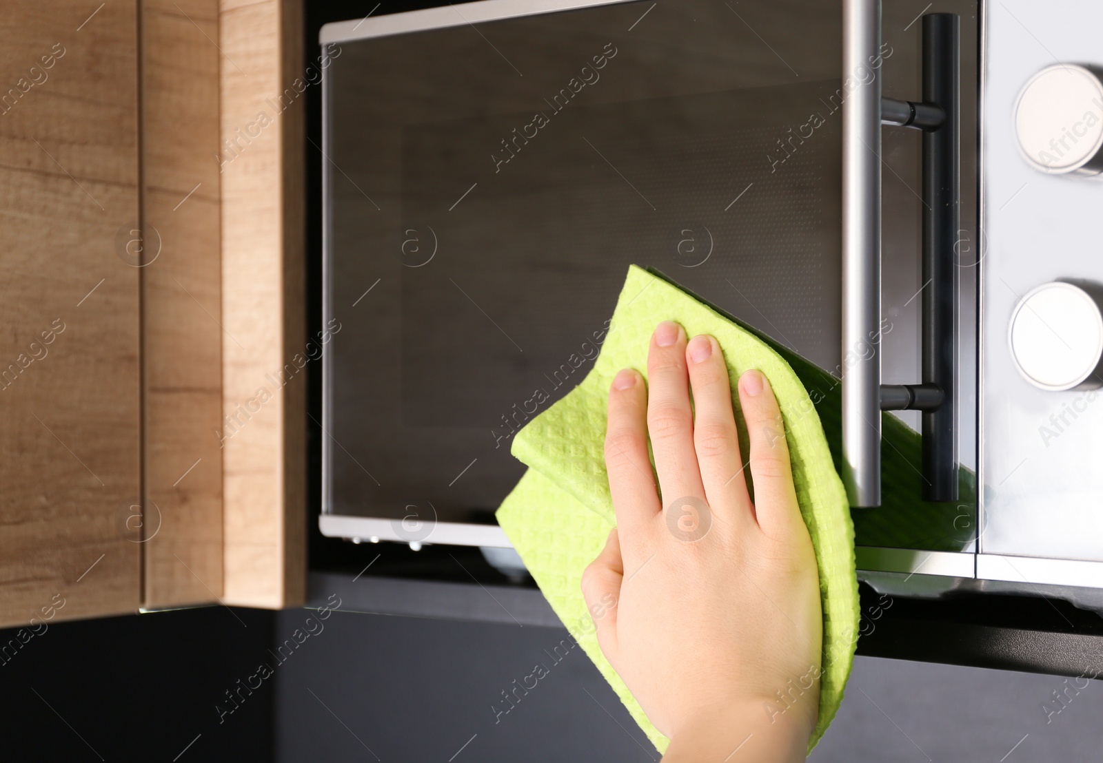 Photo of Woman cleaning microwave oven with rag in kitchen, closeup