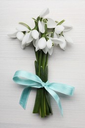 Photo of Beautiful snowdrop flowers with ribbon on white wooden table, top view