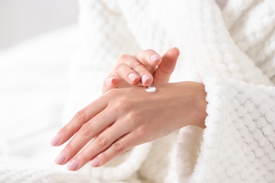 Photo of Young woman applying hand cream indoors, closeup. Beauty and body care