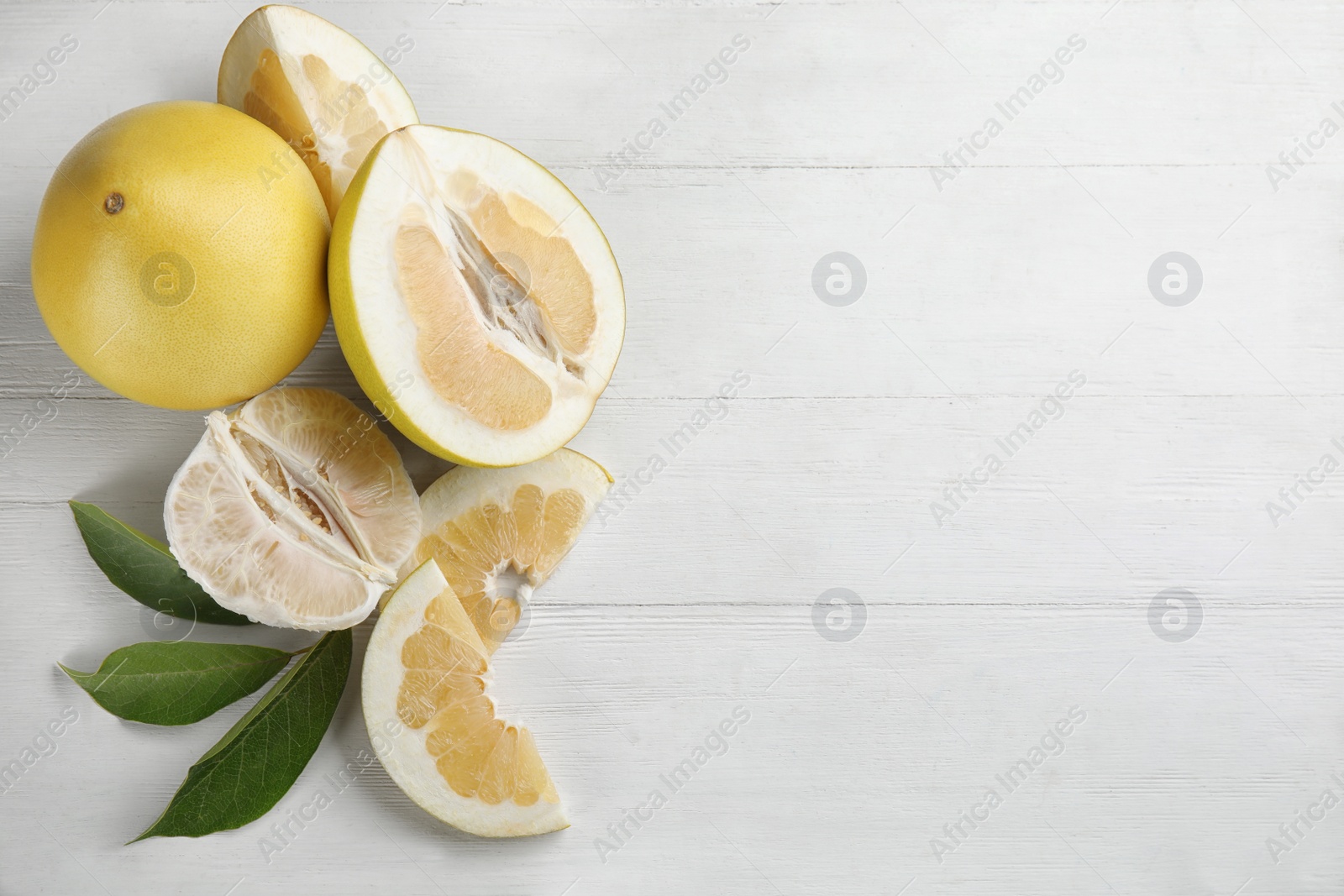 Photo of Fresh cut and whole pomelo fruits with leaves on white wooden table, flat lay. Space for text