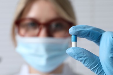 Doctor holding pill on light background, selective focus. Space for text