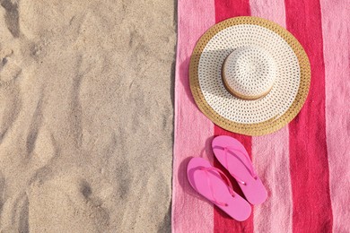 Beach towel with slippers and straw hat on sand, flat lay. Space for text