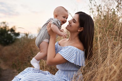 Happy mother with adorable baby in field at sunset