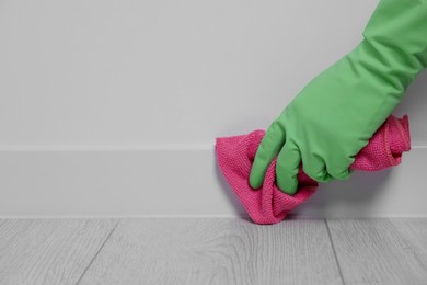 Photo of Woman in gloves cleaning plinth with cloth indoors, closeup. Space for text
