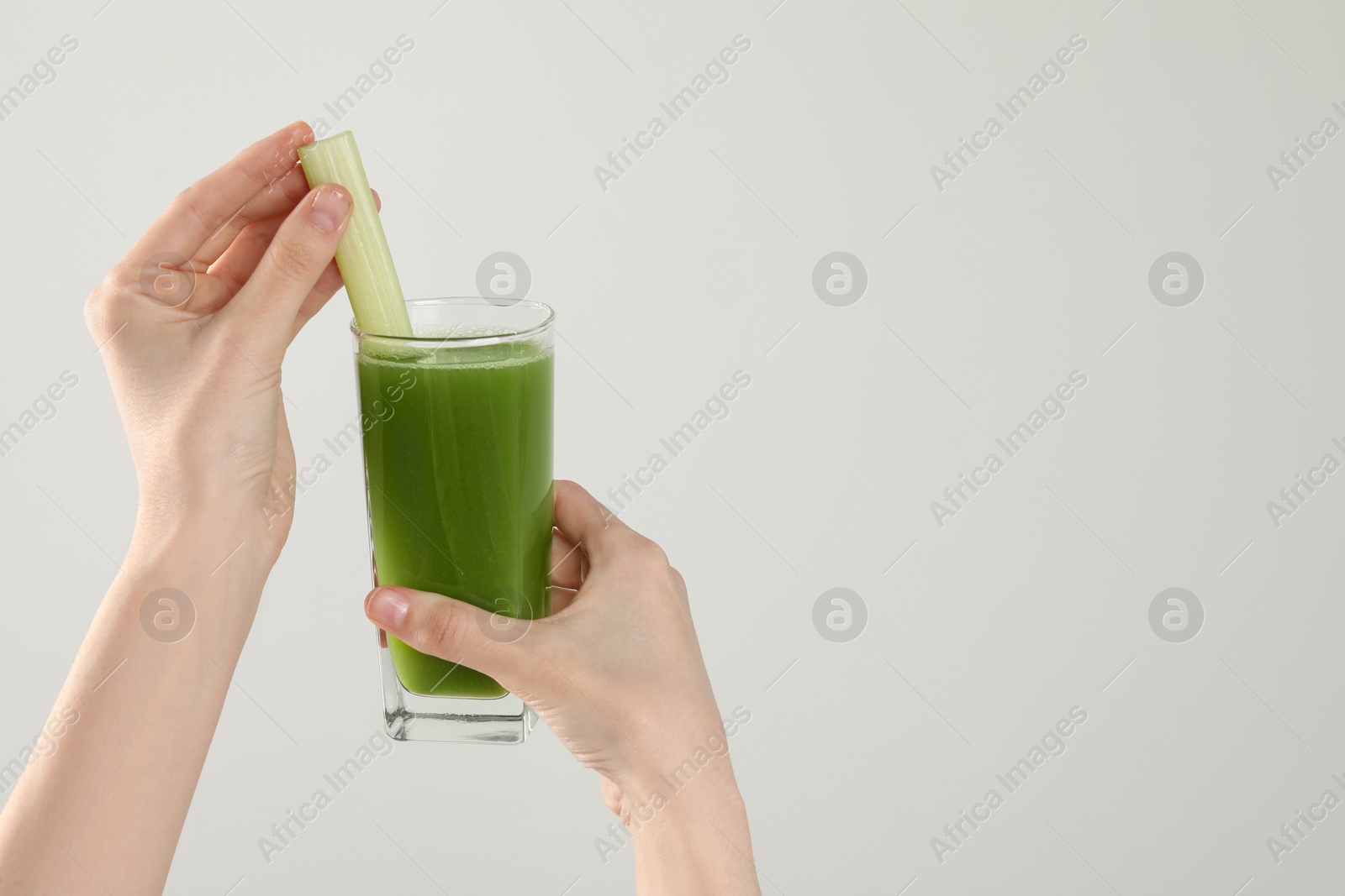 Photo of Woman holding glass of delicious celery juice on light grey background, closeup. Space for text