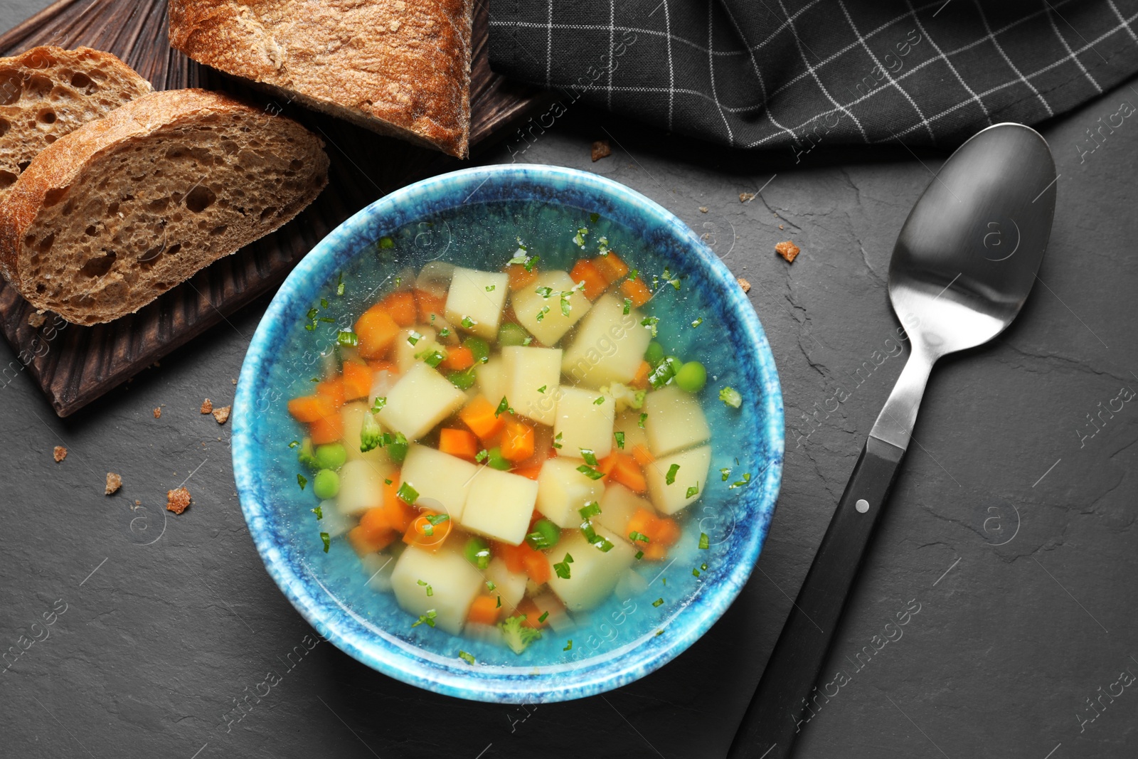 Photo of Bowl of fresh homemade vegetable soup served on black table, flat lay