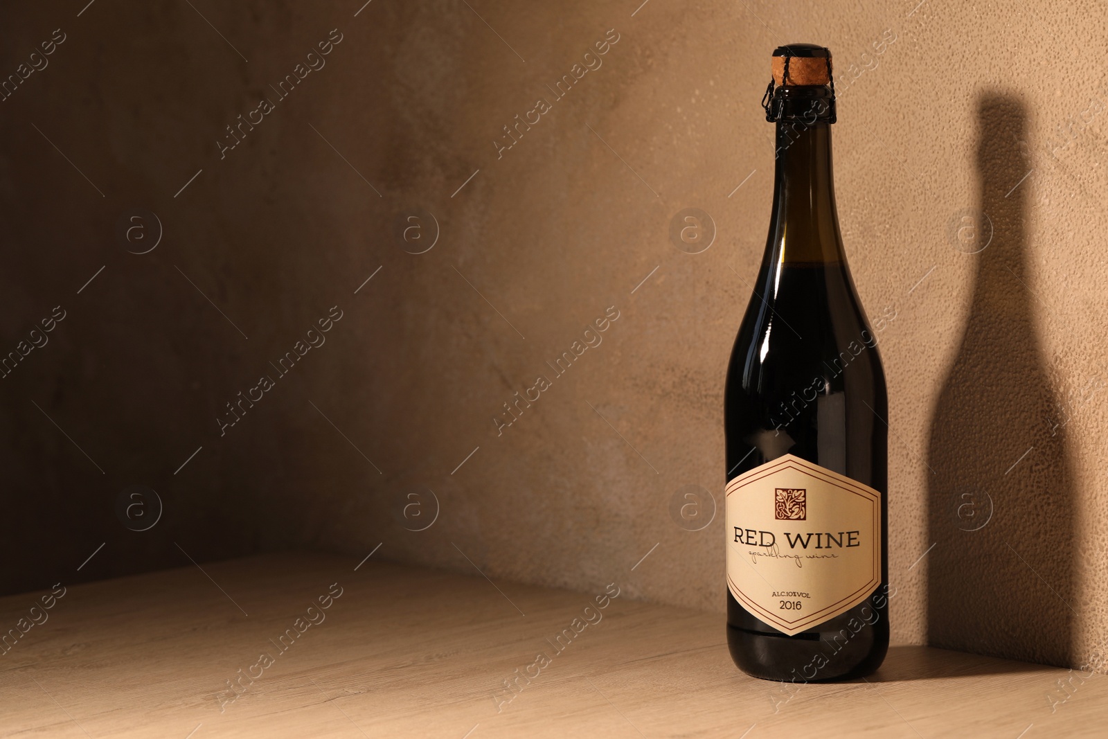 Photo of Bottle of tasty red wine on wooden table near beige wall, space for text