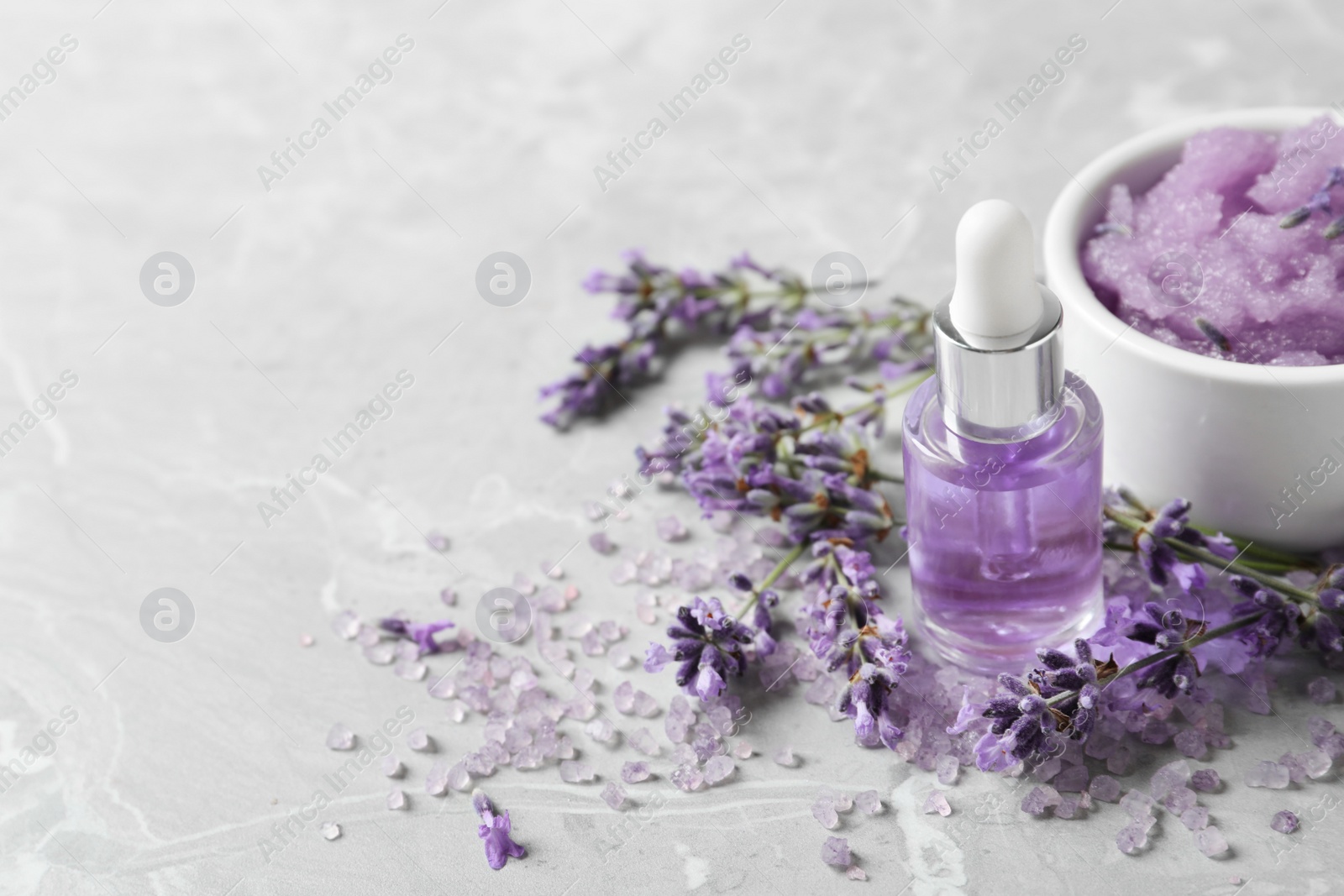 Photo of Natural cosmetic oil, bath salt, scrub and lavender flowers on grey marble table, space for text