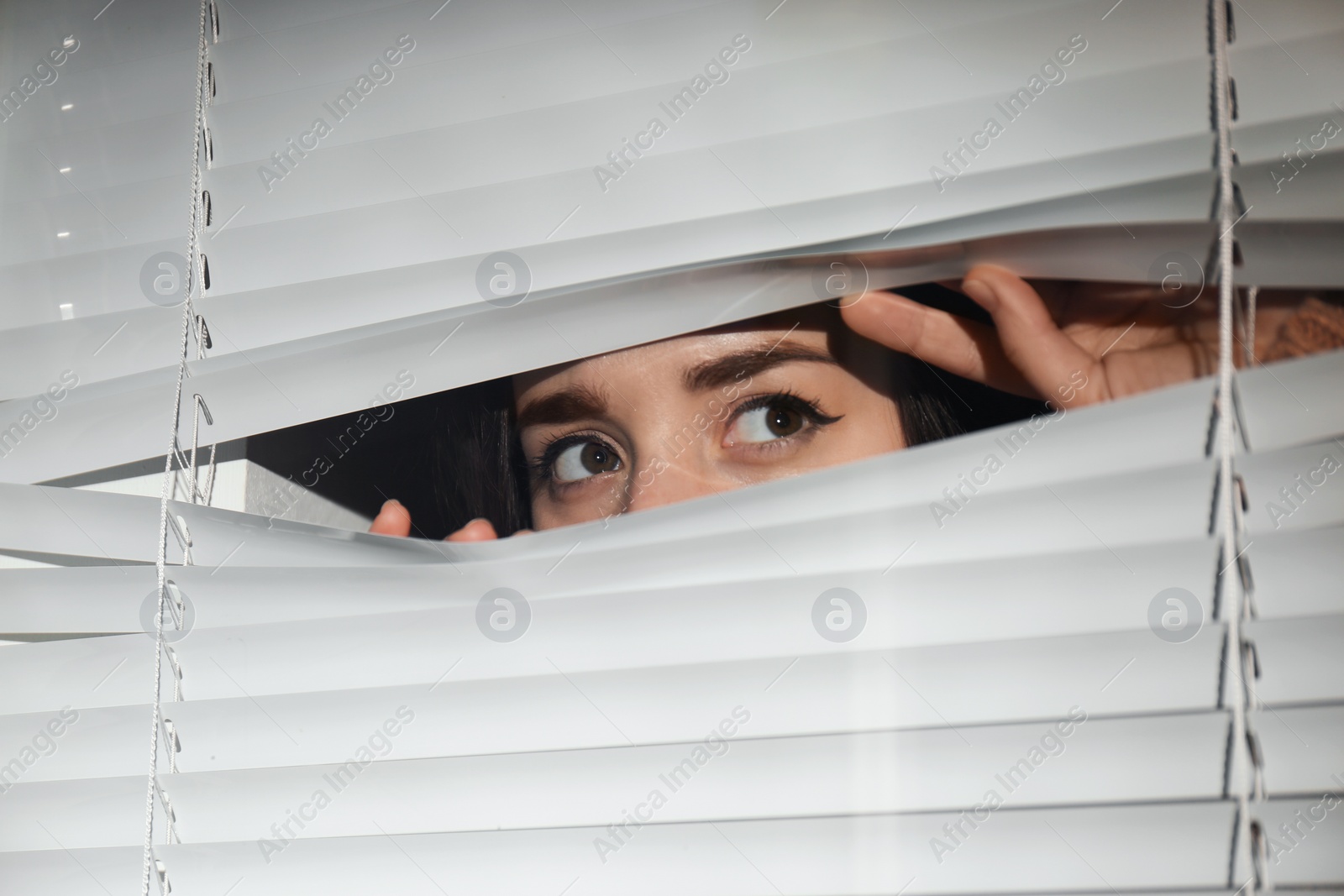 Photo of Curious woman looking through Venetian window blinds