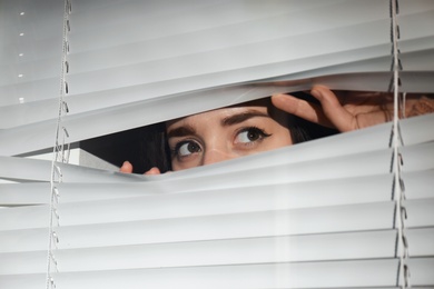 Curious woman looking through Venetian window blinds