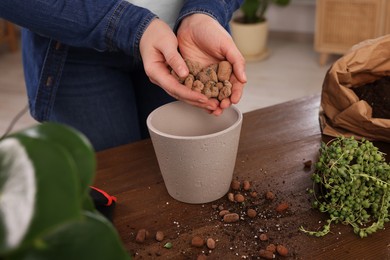 Woman filling flowerpot with drainage at wooden table indoors, closeup. Transplanting houseplants