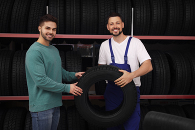 Photo of Mechanic helping client to choose car tire in auto store