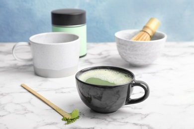 Cup of fresh beverage and matcha spoon with powdered tea on table