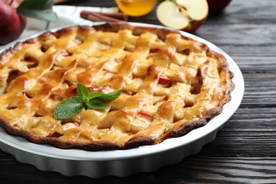 Photo of Traditional apple pie with mint on black wooden table, closeup