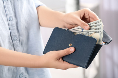 Photo of Woman putting money into wallet on blurred background, closeup