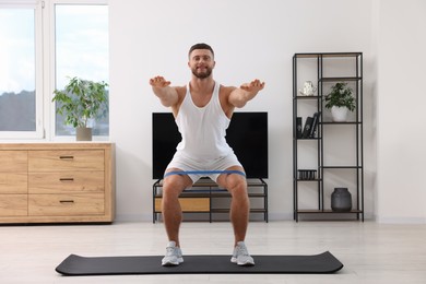 Photo of Athletic man doing exercise with elastic resistance band on mat at home