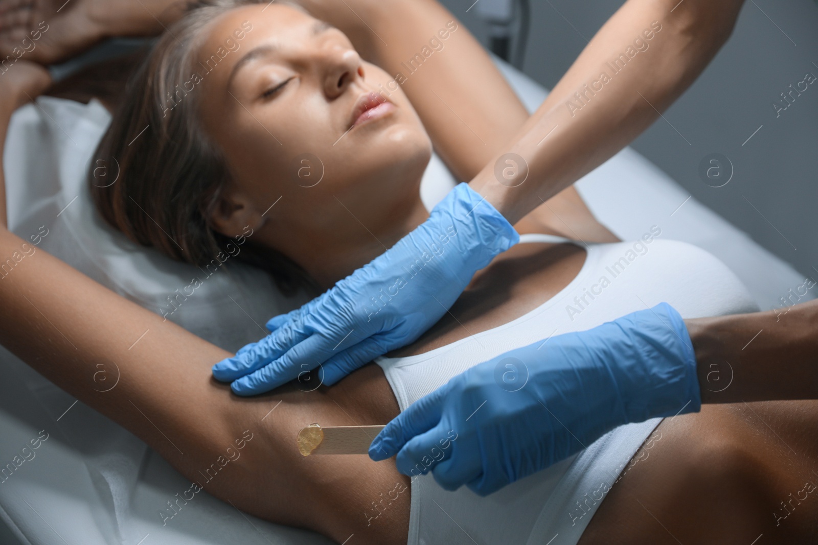 Photo of Young woman undergoing hair removal procedure of armpits with sugaring paste in salon