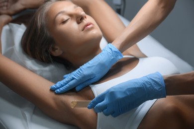 Photo of Young woman undergoing hair removal procedure of armpits with sugaring paste in salon