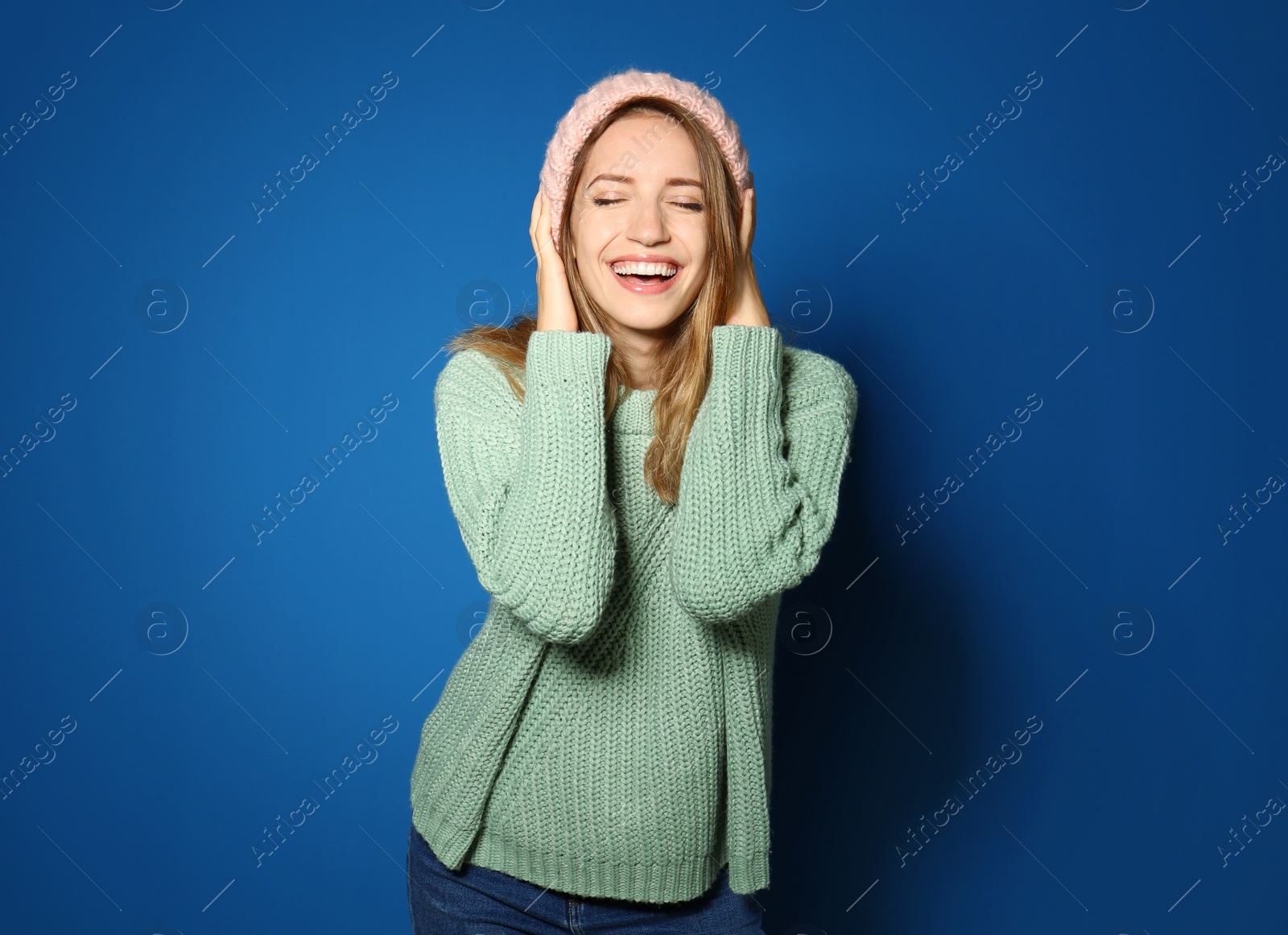 Image of Happy young woman wearing warm sweater and knitted hat on blue background