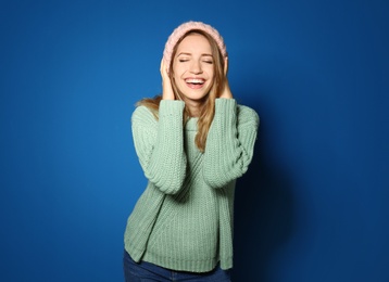 Happy young woman wearing warm sweater and knitted hat on blue background