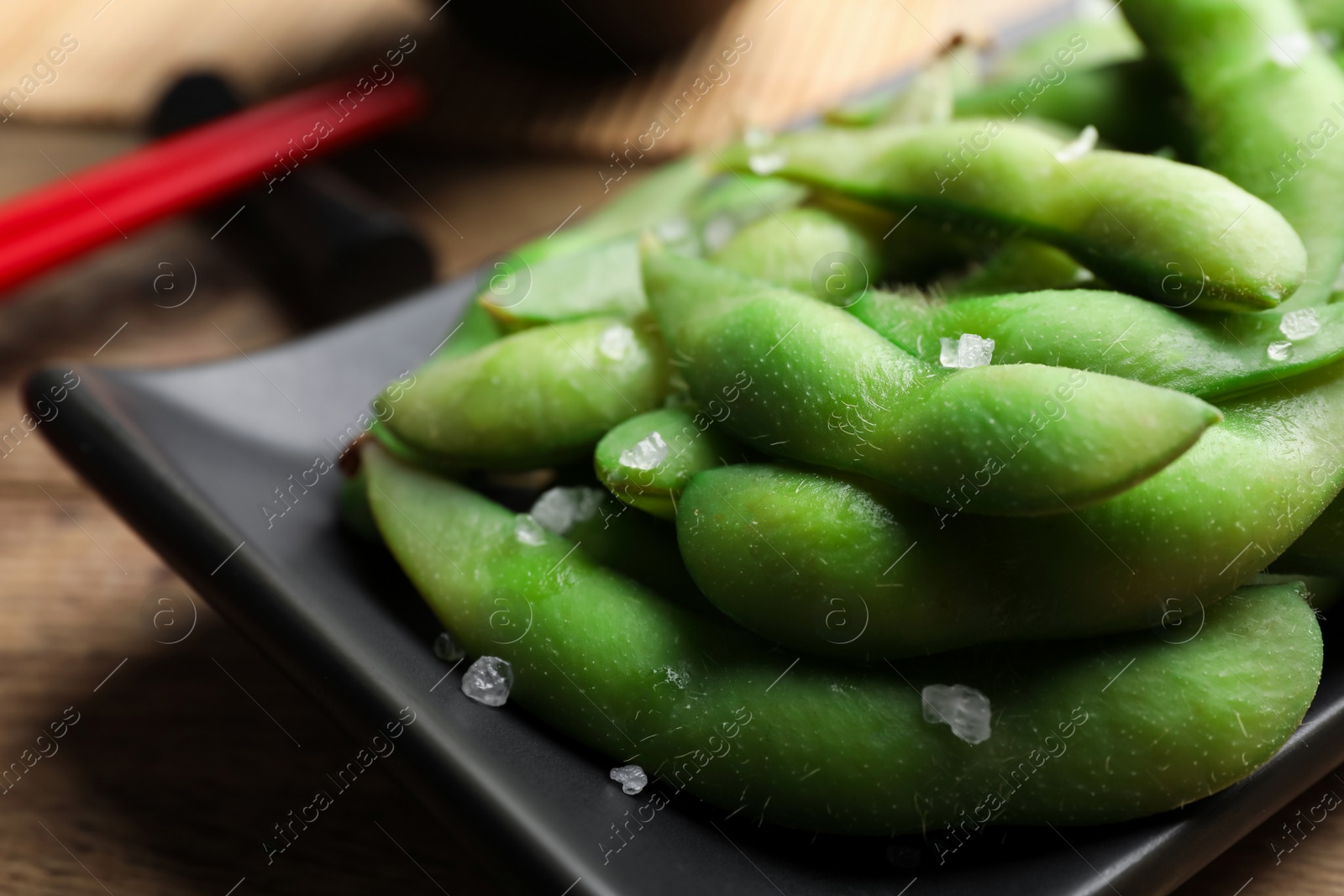 Photo of Black plate with green edamame beans in pods on wooden table, closeup