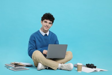 Portrait of student with laptop and stationery on light blue background