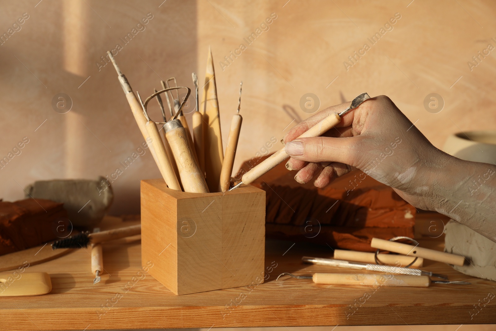 Photo of Woman taking clay crafting tool from wooden holder in workshop, closeup