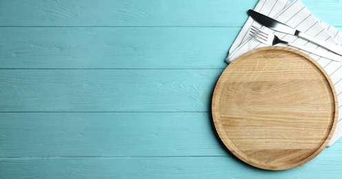 Photo of Wooden plate with cutlery and napkin on light blue table, flat lay. Space for text