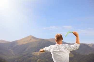 Photo of Man throwing boomerang in mountains on sunny day, back view. Space for text