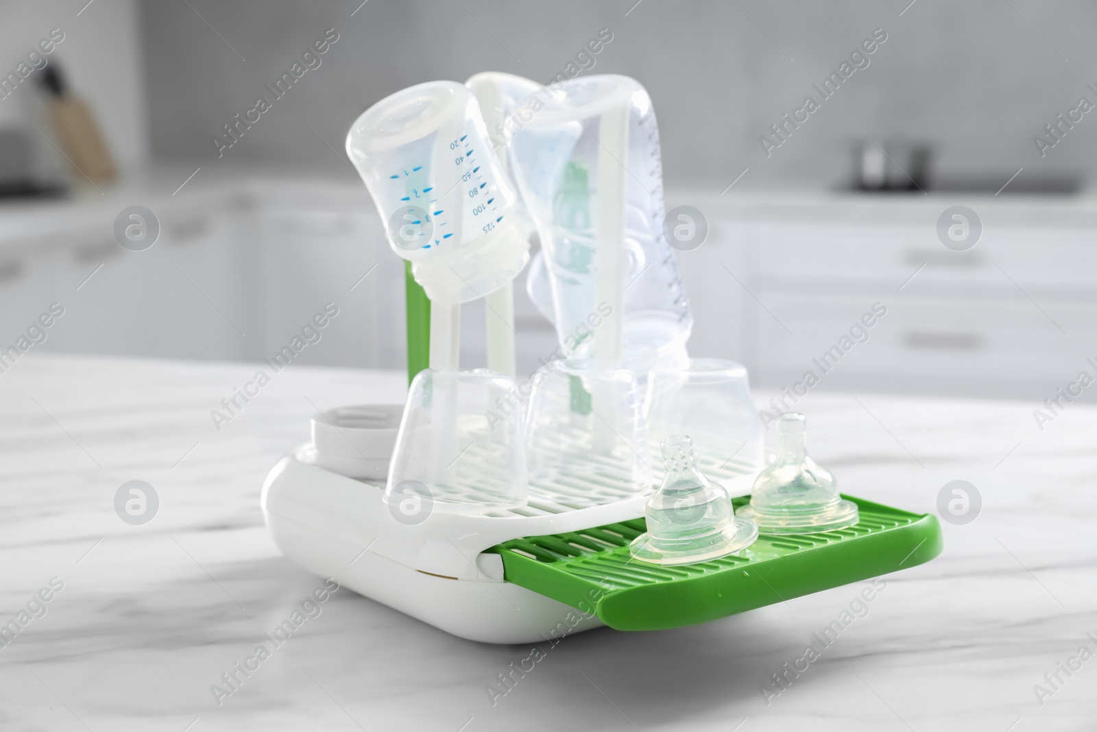 Photo of Dryer with baby bottles and nipples after sterilization on white marble table in kitchen